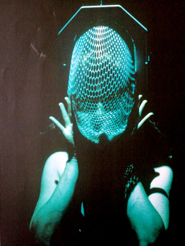Aimee Greenberg as Lilith holding a face net mask.