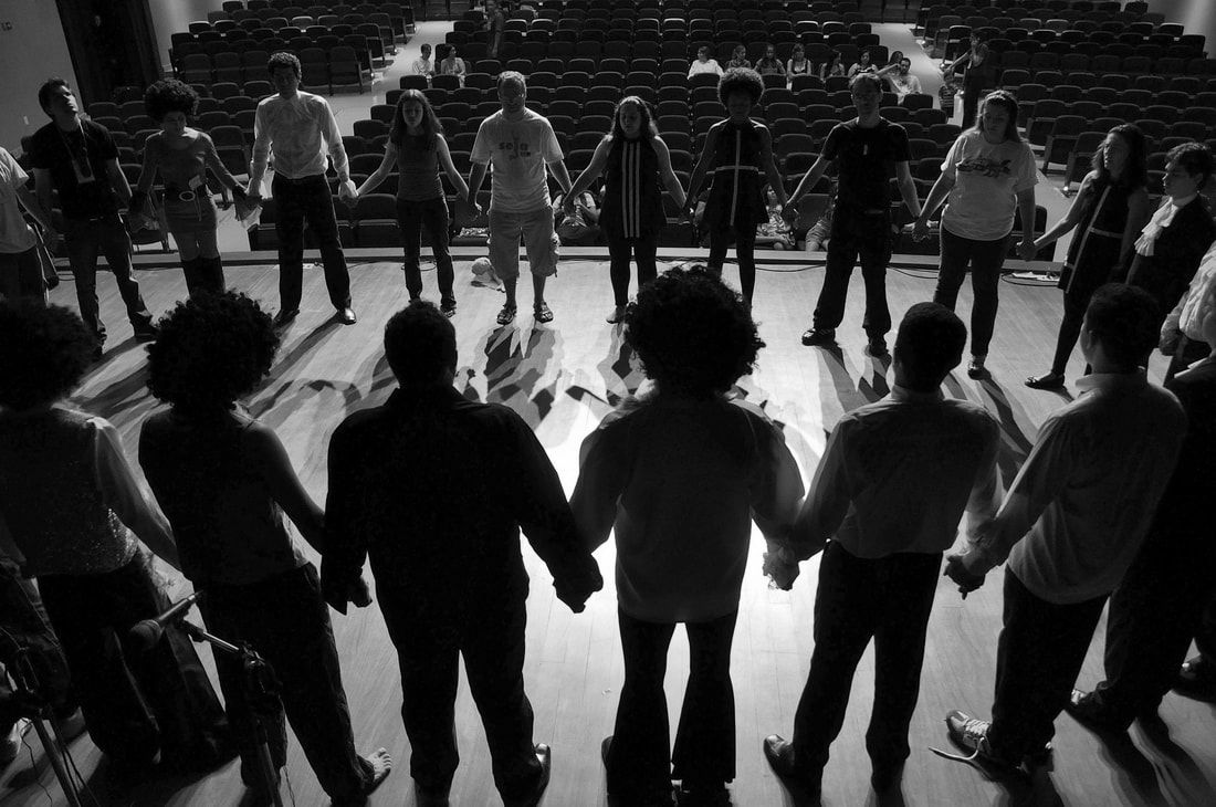 Color photo of young actors on stage holding hands in a circle.